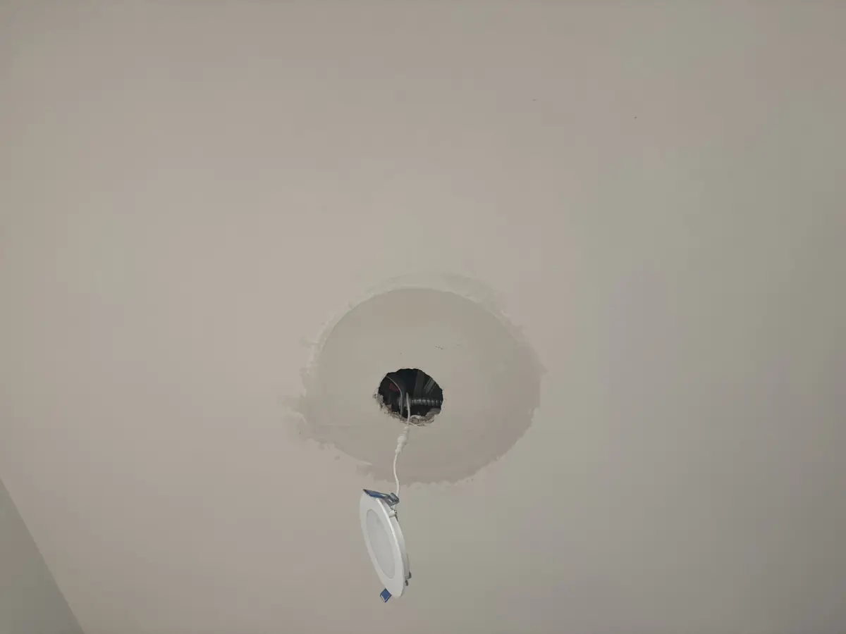 Drywall patch around a recessed can light in a ceiling, ready for finishing