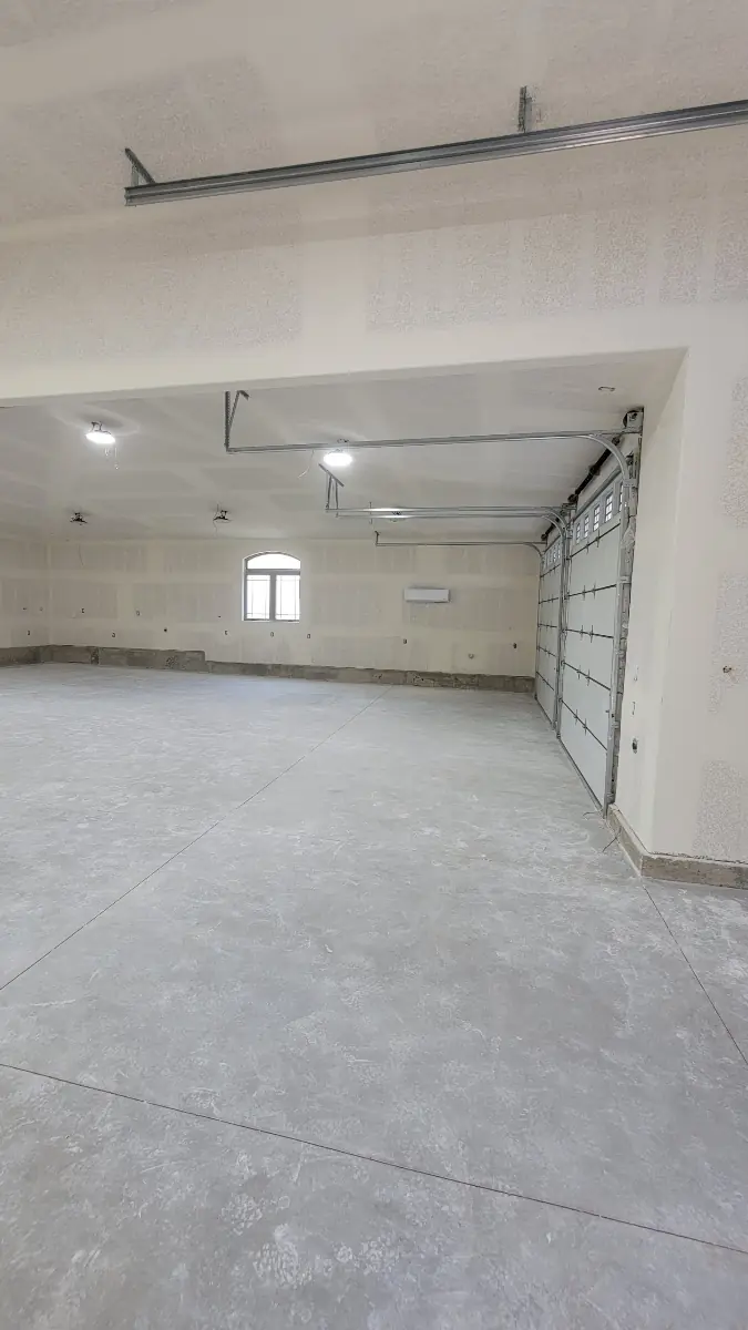 Drywalled garage ceiling with conduit and recessed lighting above a finished concrete floor